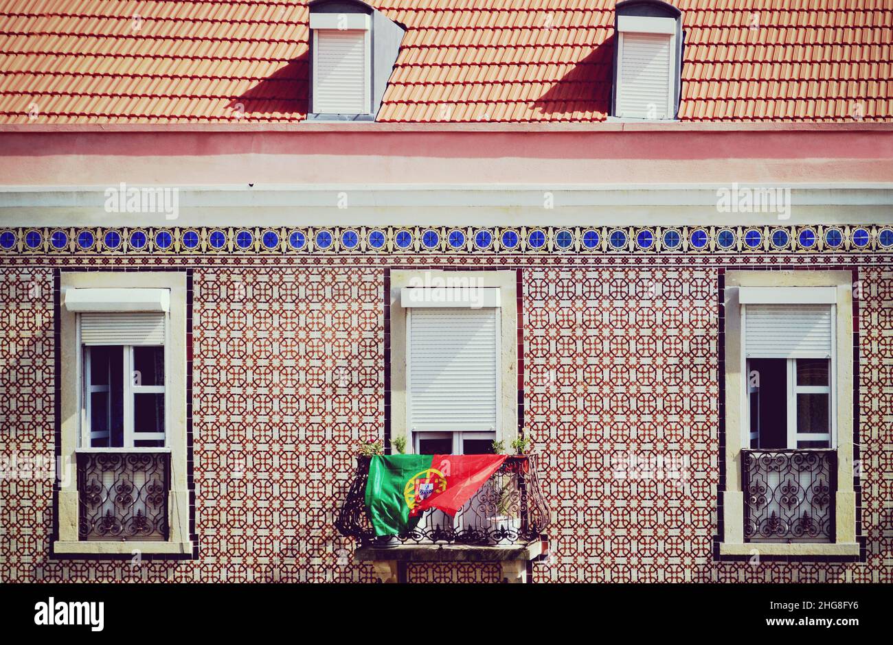 Facciata di un edificio a Lisbona, con iconici azulejos o piastrelle di ceramica e una bandiera ondulata del Portogallo appesa alla finestra Foto Stock