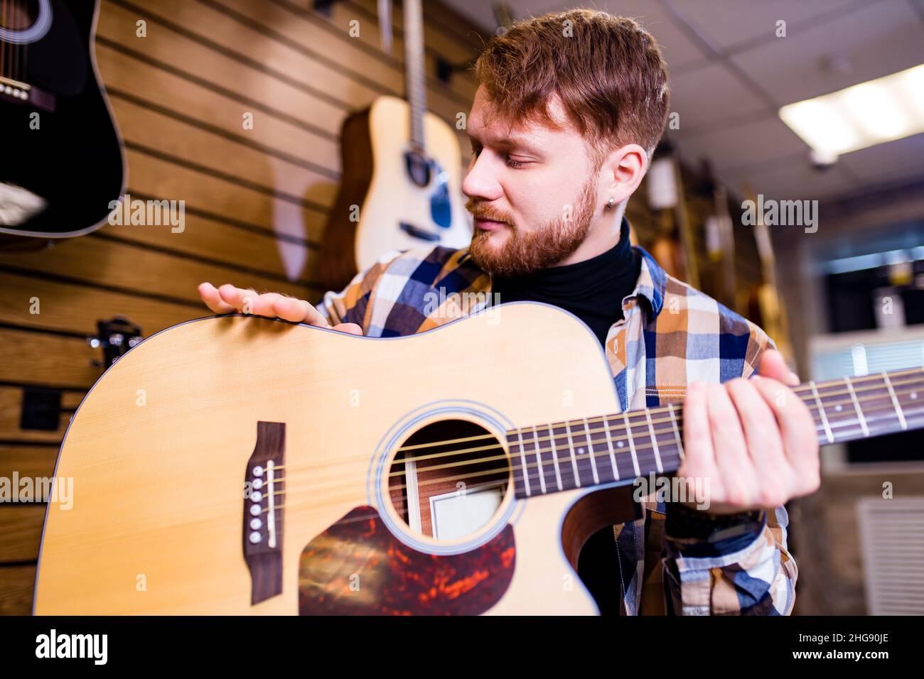 l'uomo dello zenzero redhairs sta scegliendo la chitarra acustica di qualità nel negozio di chitarra Foto Stock