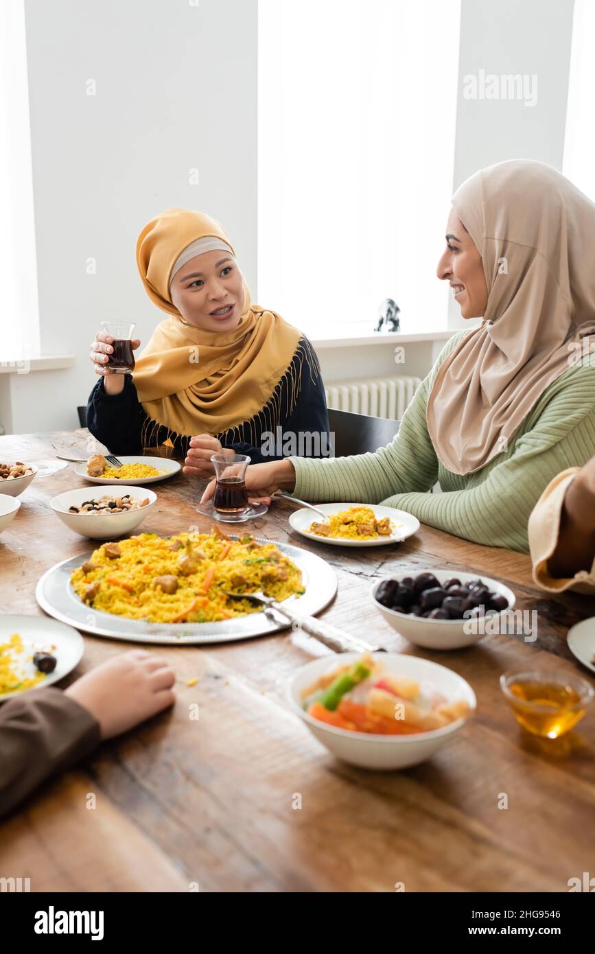 donna musulmana asiatica che tiene un bicchiere di tè vicino alla figlia araba durante la cena di famiglia Foto Stock