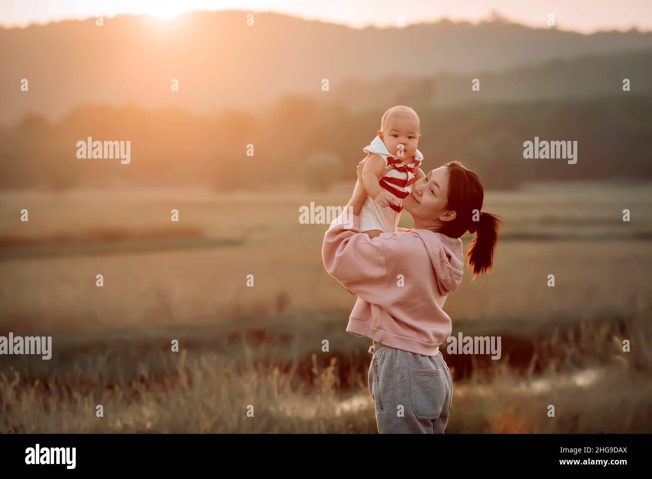 Ritratto di una donna sorridente in piedi in un campo che tiene il suo bambino ragazzo, Sakon Nakhon, Isan, Thailandia Foto Stock