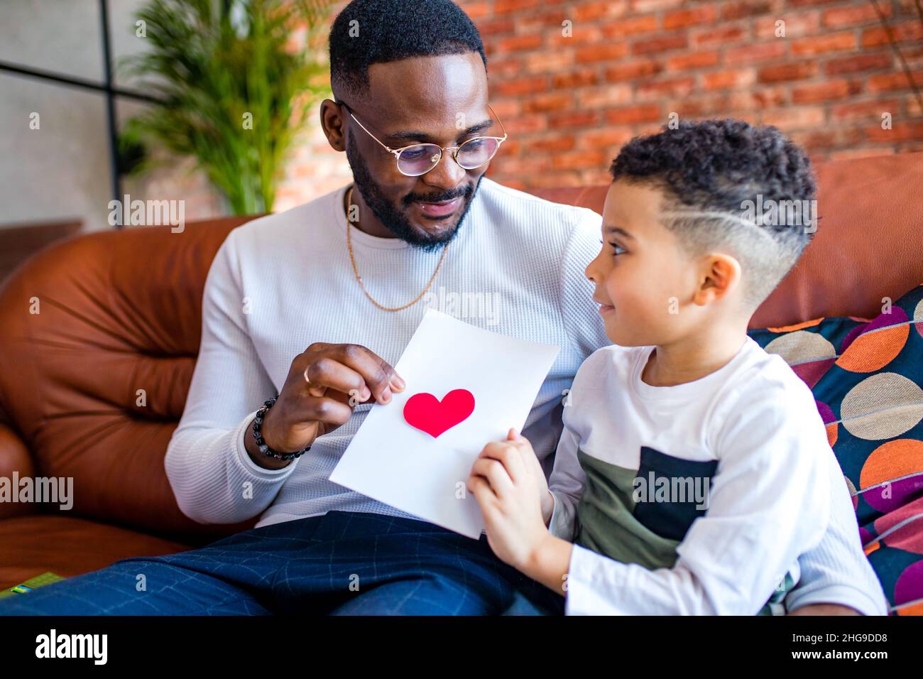 afro bambino americano che dà al papà un'immagine di giorno di San Valentino in salotto Foto Stock