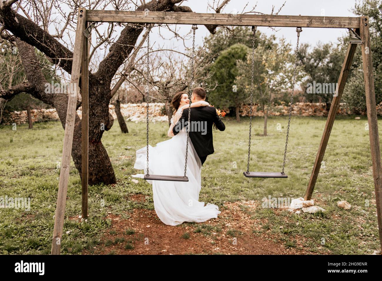 Felice coppia sorridente di stile che cammina in Toscana, Italia il giorno del matrimonio. SPOSI NOVELLI CON L'ALTALENA NEL PARCO. La sposa e lo sposo camminano giù il Foto Stock