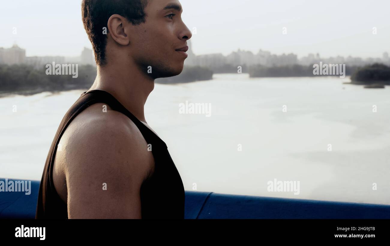 vista laterale del giovane uomo birazziale sul ponte della città sul fiume, immagine di stock Foto Stock