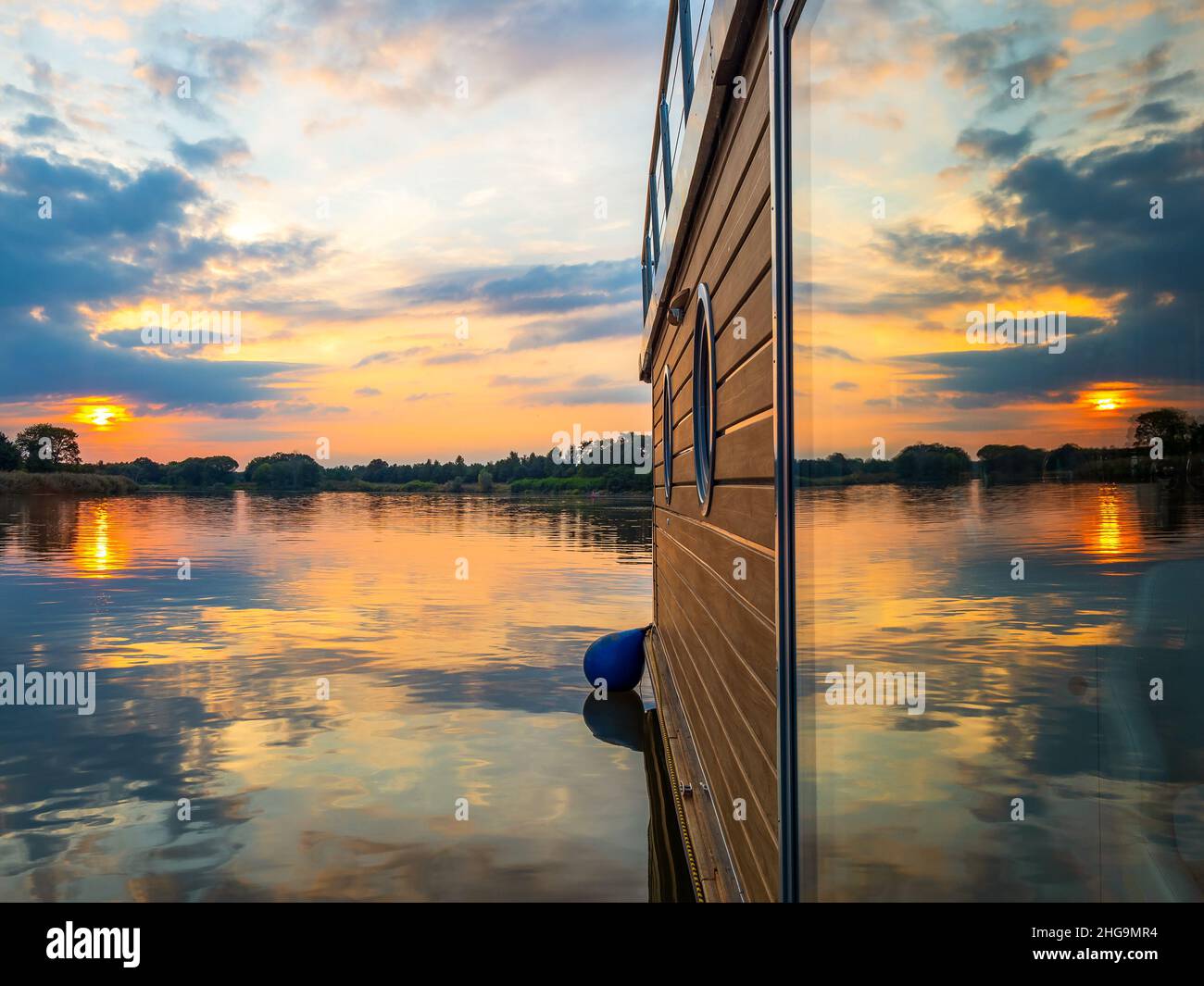 Tramonto dietro casa galleggiante su un fiume. Il tramonto si riflette in una finestra di una casa galleggiante in una calda serata estiva Foto Stock