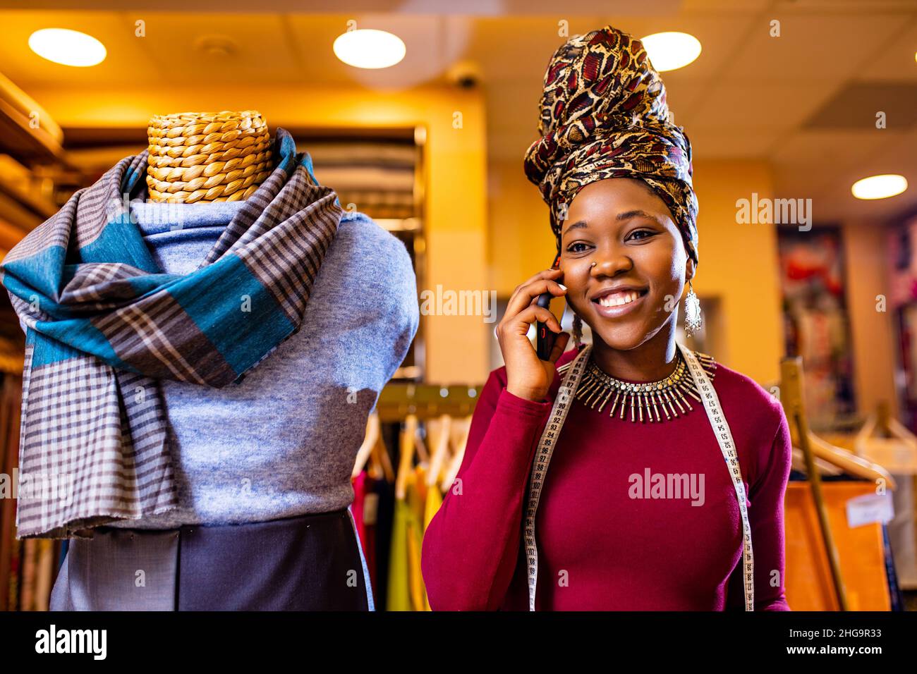 donna tanzaniana con serpente stampa turban oltre sentire lavorare in negozio di tessuti chiamata al cliente da smartphone Foto Stock