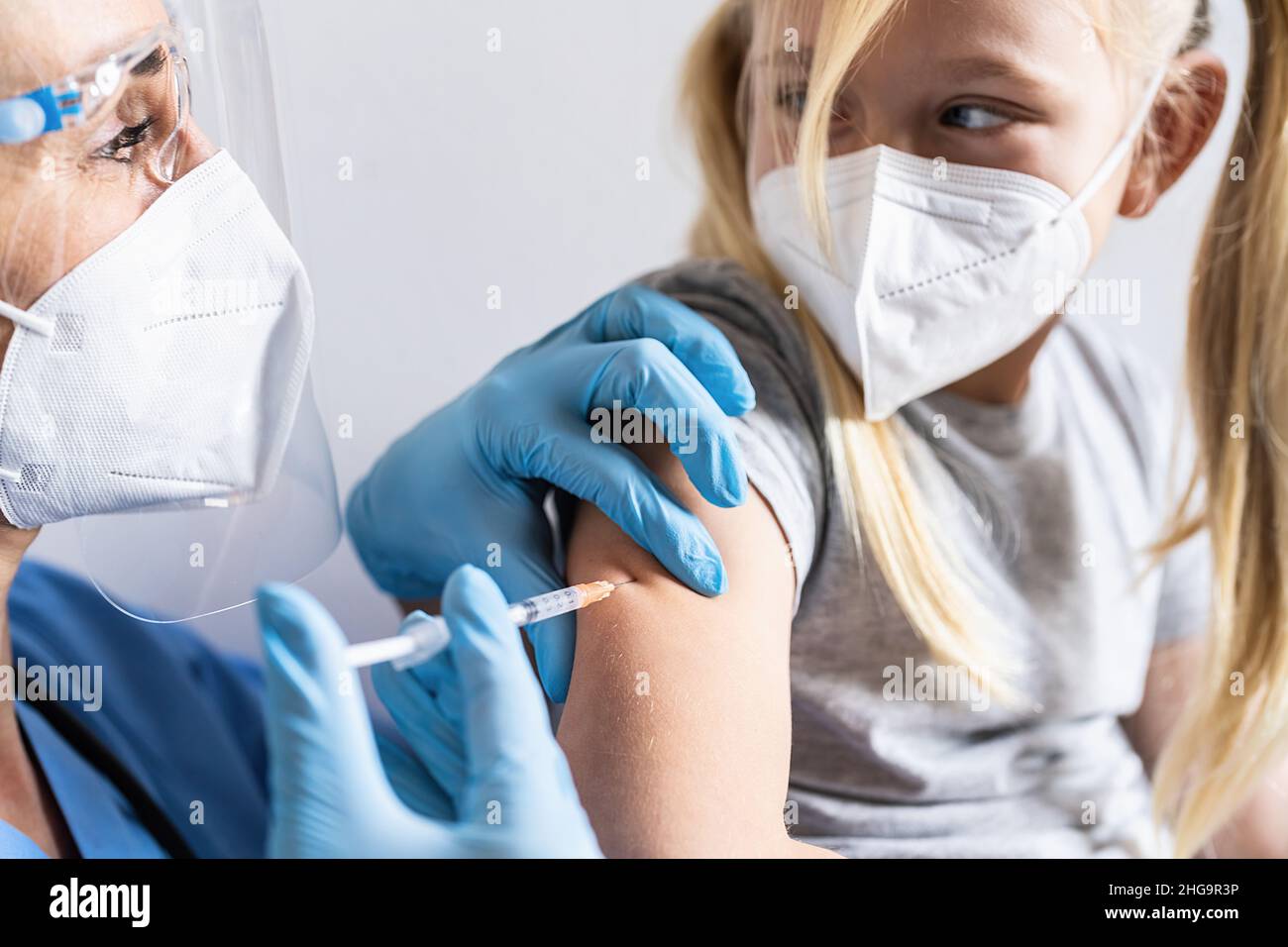 Bambina in maschera in ufficio medico ottenere vaccinato. Siringa con vaccino per il co-virus-19 coronavirus, influenza, malattie infettive pericolose. Injetti Foto Stock