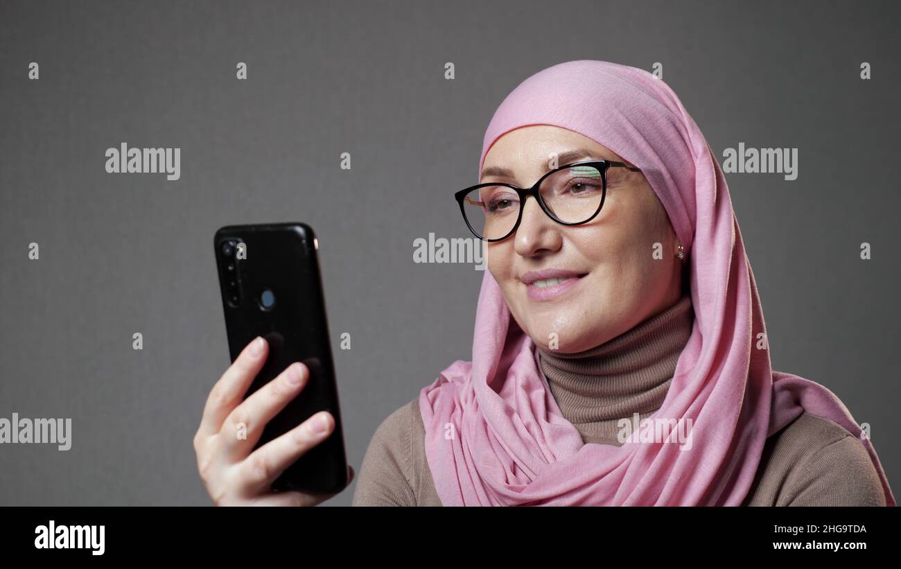 La giovane donna musulmana in hijab sorride guardando lo spettacolo al telefono Foto Stock