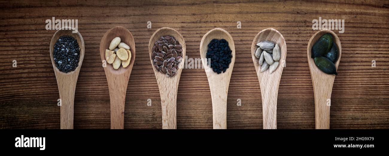 Set di semi organici in cucchiai su sfondo panoramico in legno, cibo naturale sano e concetto di nutrizione Foto Stock