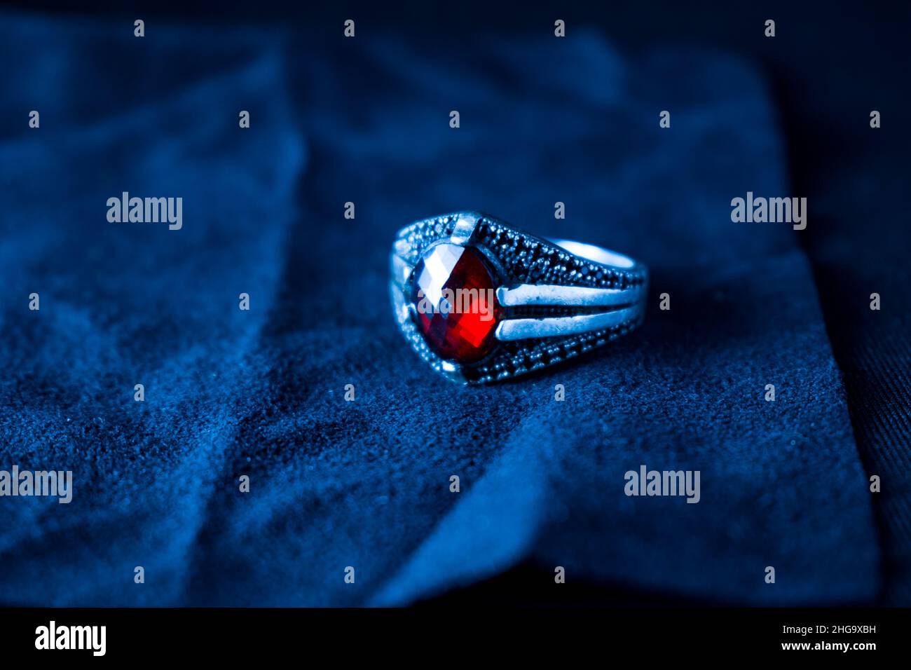 Un'immagine ravvicinata di un anello d'argento con pietra rossa su sfondo blu Foto Stock