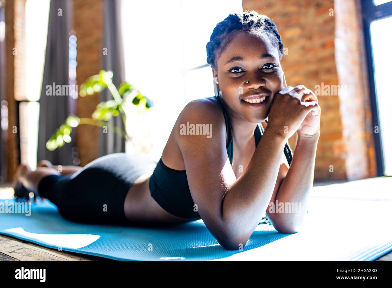 donna ispanica con capelli afro pigtail ascolto di una musica da wireless auricolari pods indossare abiti sportivi nero reggiseno e leggings al sole giorno al chiuso Foto Stock