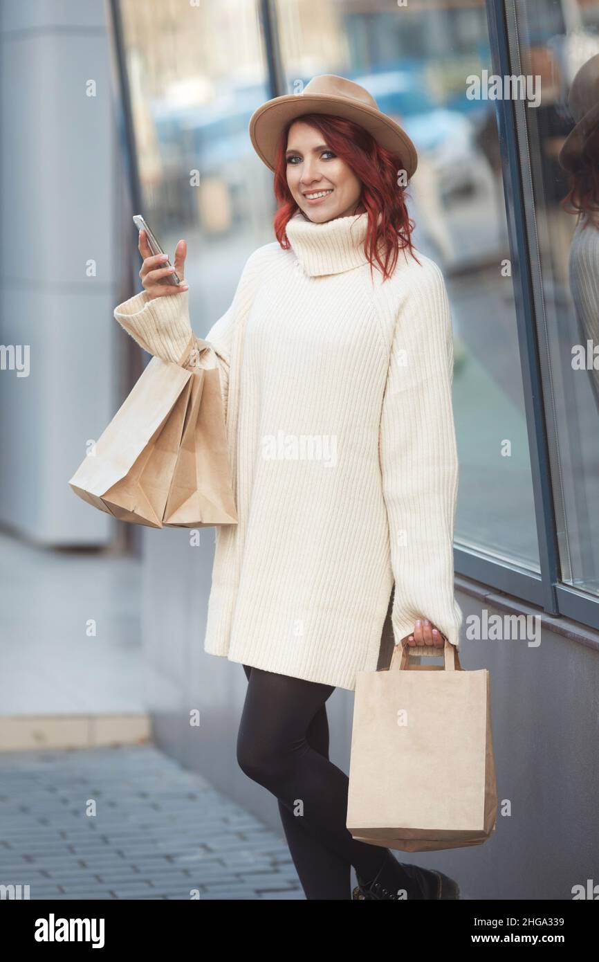 Street stile portrai di donna di moda felice millennial con molti sacchi di artigianato dopo lo shopping di vendita in piedi accanto all'ingresso del centro commerciale Foto Stock