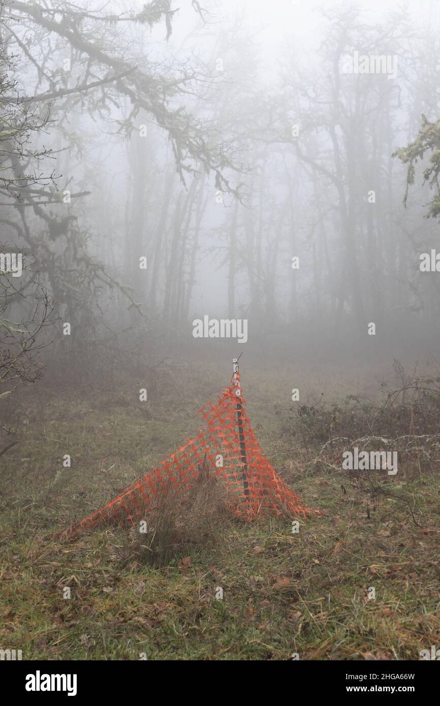 Una sezione di vecchia recinzione plastica temporanea arancione poggiata su un palo di metallo in un cantiere. Foto Stock