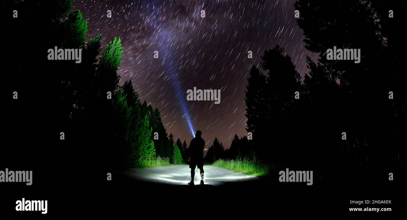 Uomo in piedi nel buio con le stelle con torcia a forest cielo notturno Foto Stock