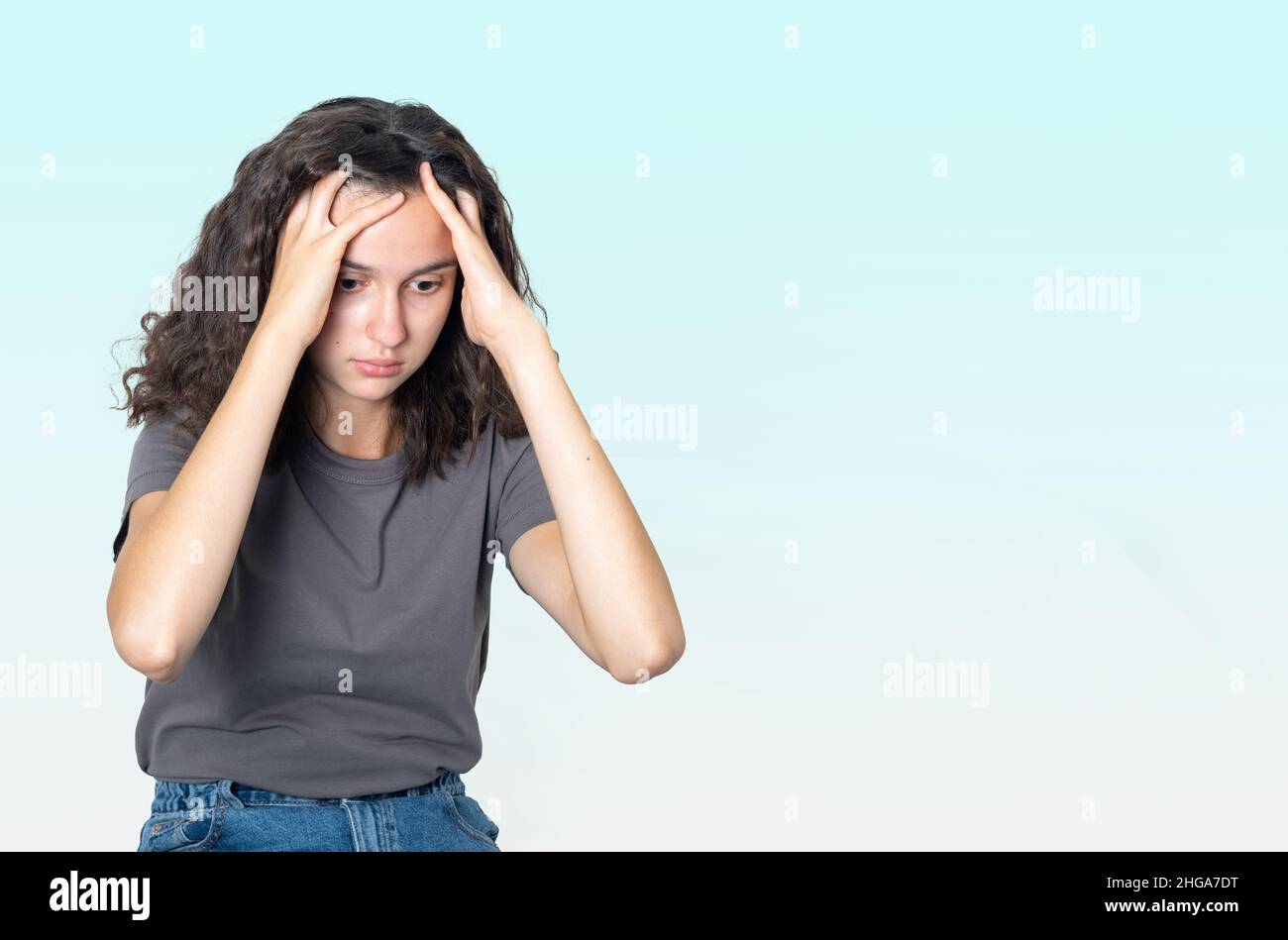 Concetto di salute mentale. Turbata ragazza triste adolescente che soffre di solitudine, tenendo la testa con le mani su uno sfondo blu gradiente, copia spazio. U Foto Stock