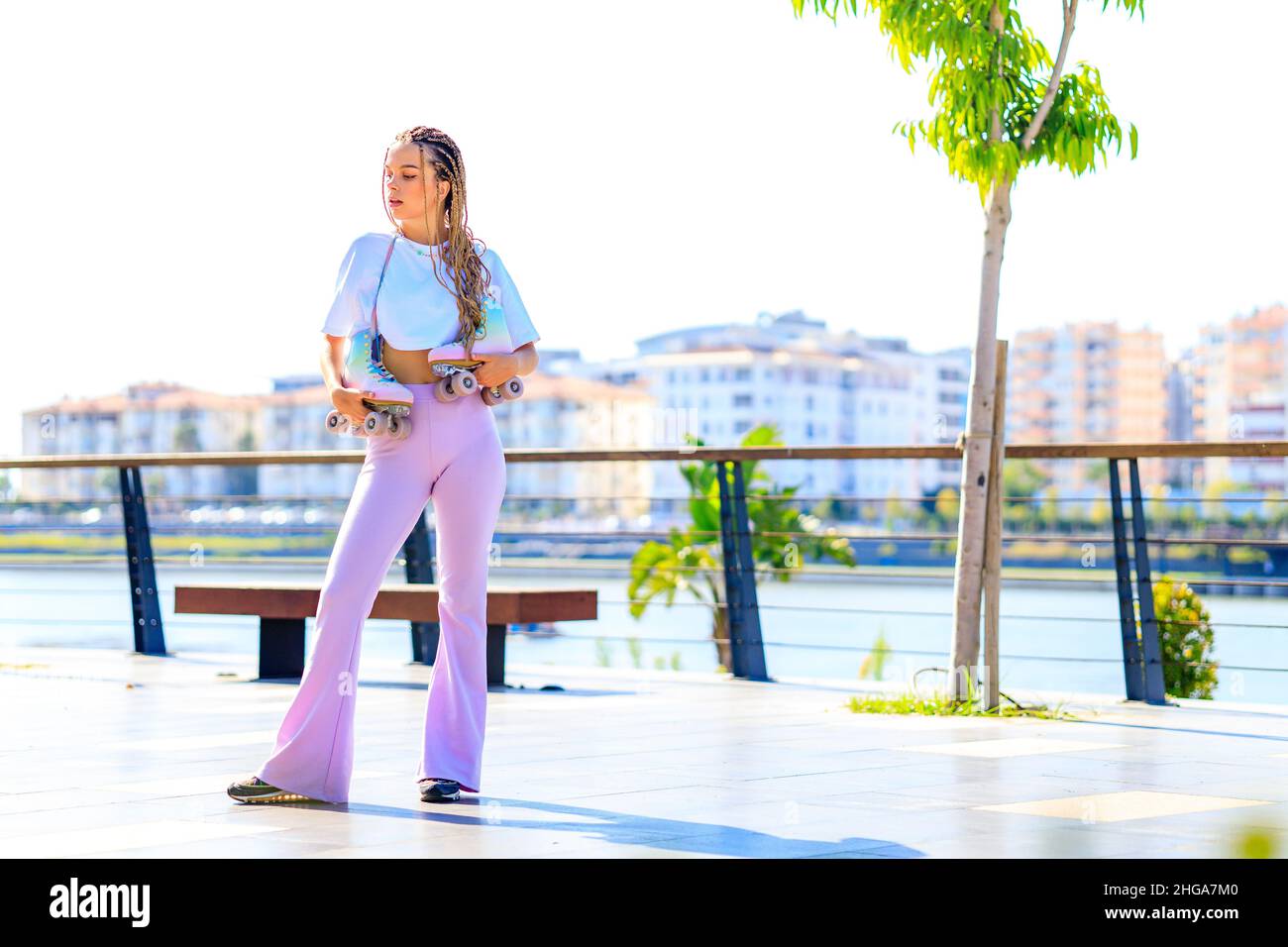 Ritratto di bella ragazza bionda adolescente con cool pigtail, maglietta bianca e pantaloni rosa flared pattinaggio su rulli nel parco Foto Stock