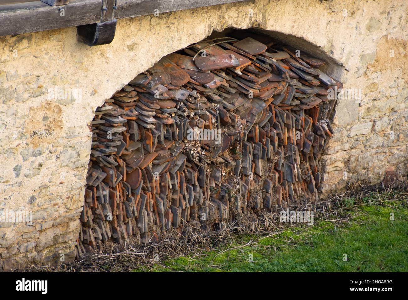 Vista inclinata di vecchie tegole del tetto immagazzinate in un'incavatura di un vecchio muro di pietra Foto Stock
