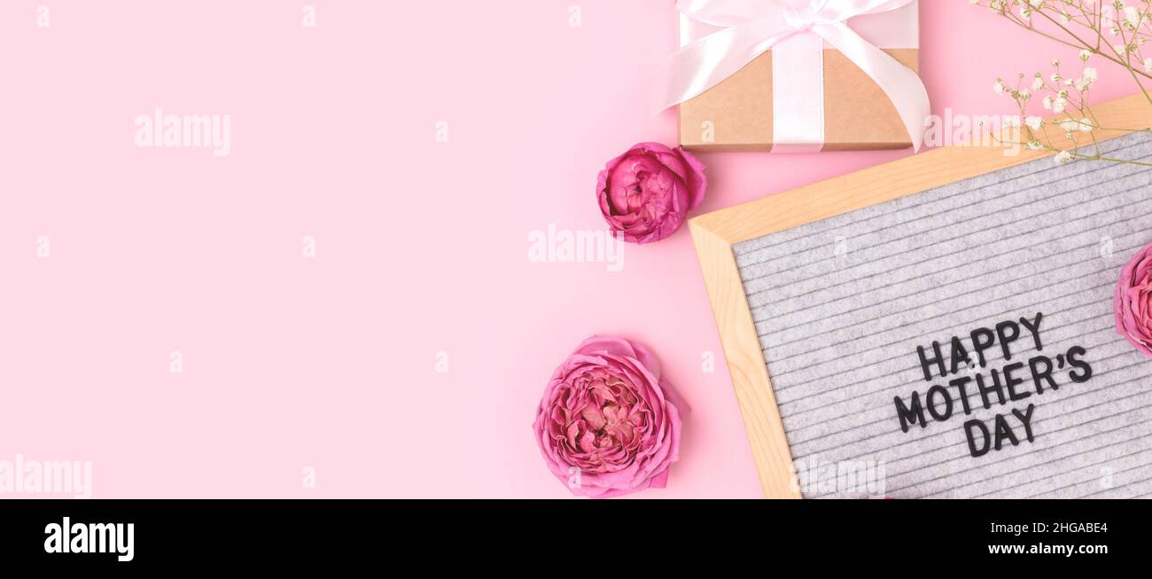 Buon giorno delle madri. Banner con cartellone, gypsofila e fiori di rosa, regalo legato con nastro su sfondo rosa. Foto Stock