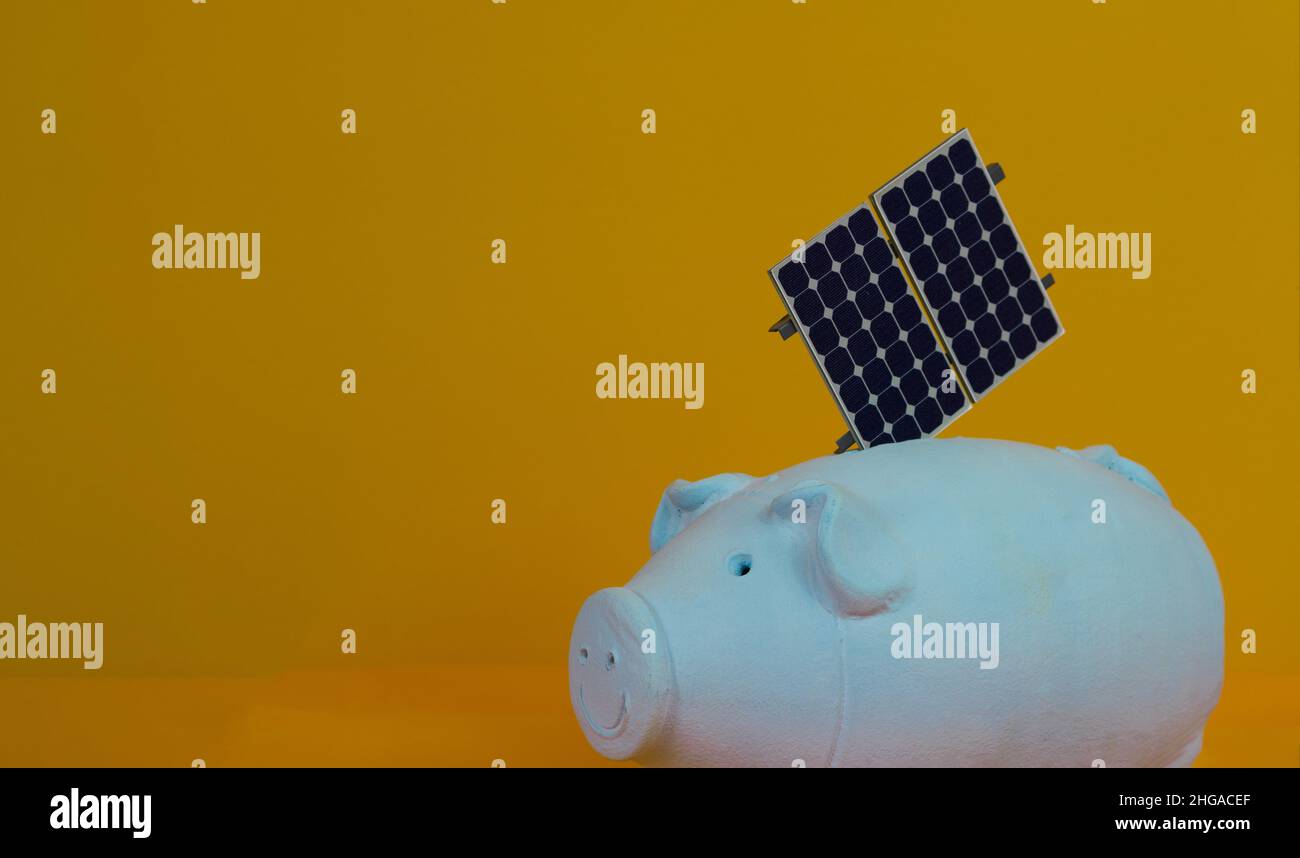 Piggy bank e fotovoltaico pannello di energia solare isolato su sfondo giallo. Foto Stock