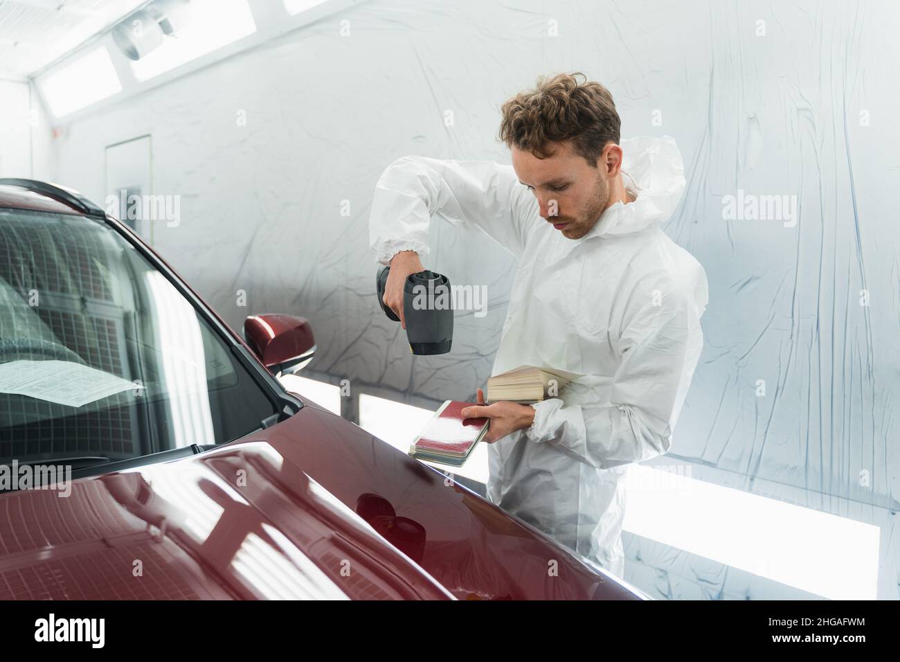 L'uomo pittore determina la tonalità corretta del colore della carrozzeria di un veicolo utilizzando una lampada speciale. Autorimessa in garage Foto Stock