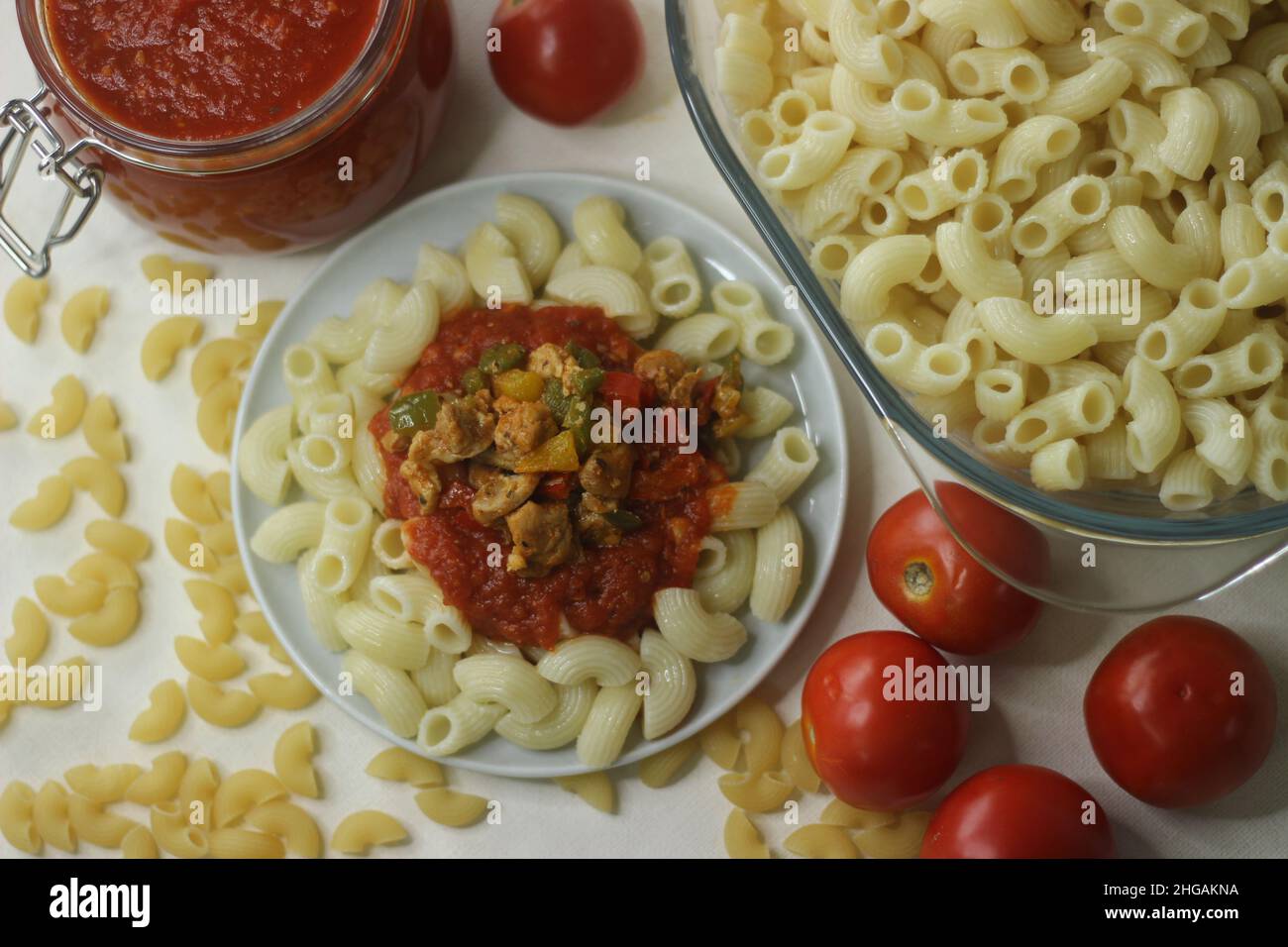 La pasta di maccheroni viene servita con salsa rossa e pollo saltato e peperoni in cima. Sparare con la pasta bollita di maccheroni in un recipiente di vetro, la salsa rossa in un bicchiere Foto Stock