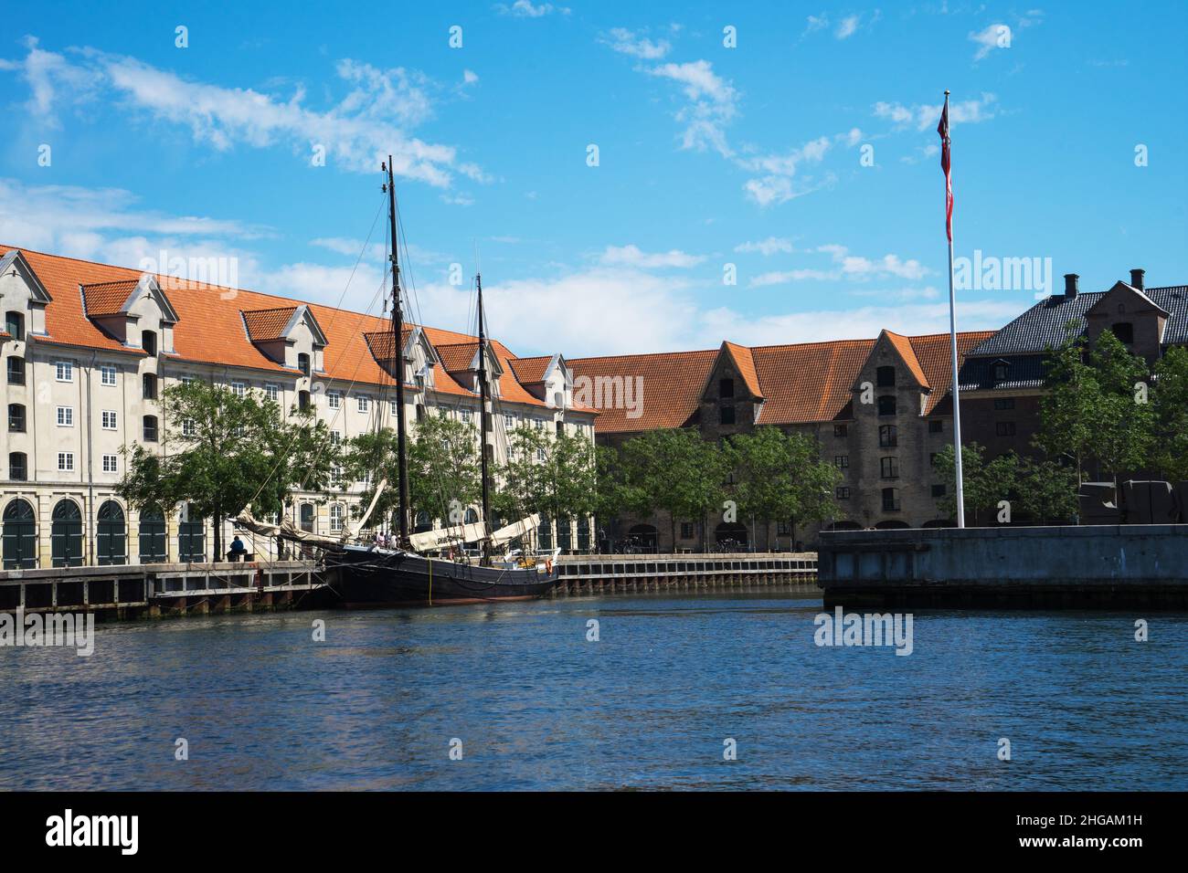 Vista sul lungomare di Copenhagen, Danimarca, vecchie case con tetti di tegole e una nave a vela con vele abbassate su un molo di legno in una giornata estiva soleggiata. Foto Stock