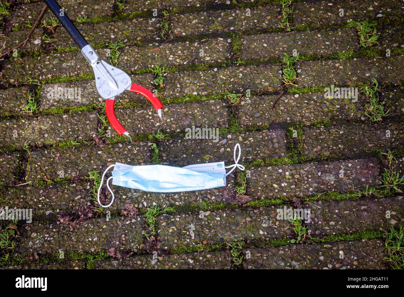 Primo piano dello strumento Grabber Reacher informazioni sulla raccolta della maschera usata per il viso gettata a terra, concetto di pulizia ambientale Foto Stock
