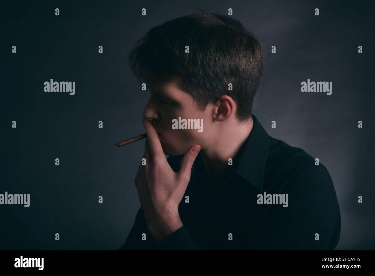 L'uomo fuma un sigaro. Ragazzo fumando sigaretta su sfondo scuro. Foto Stock