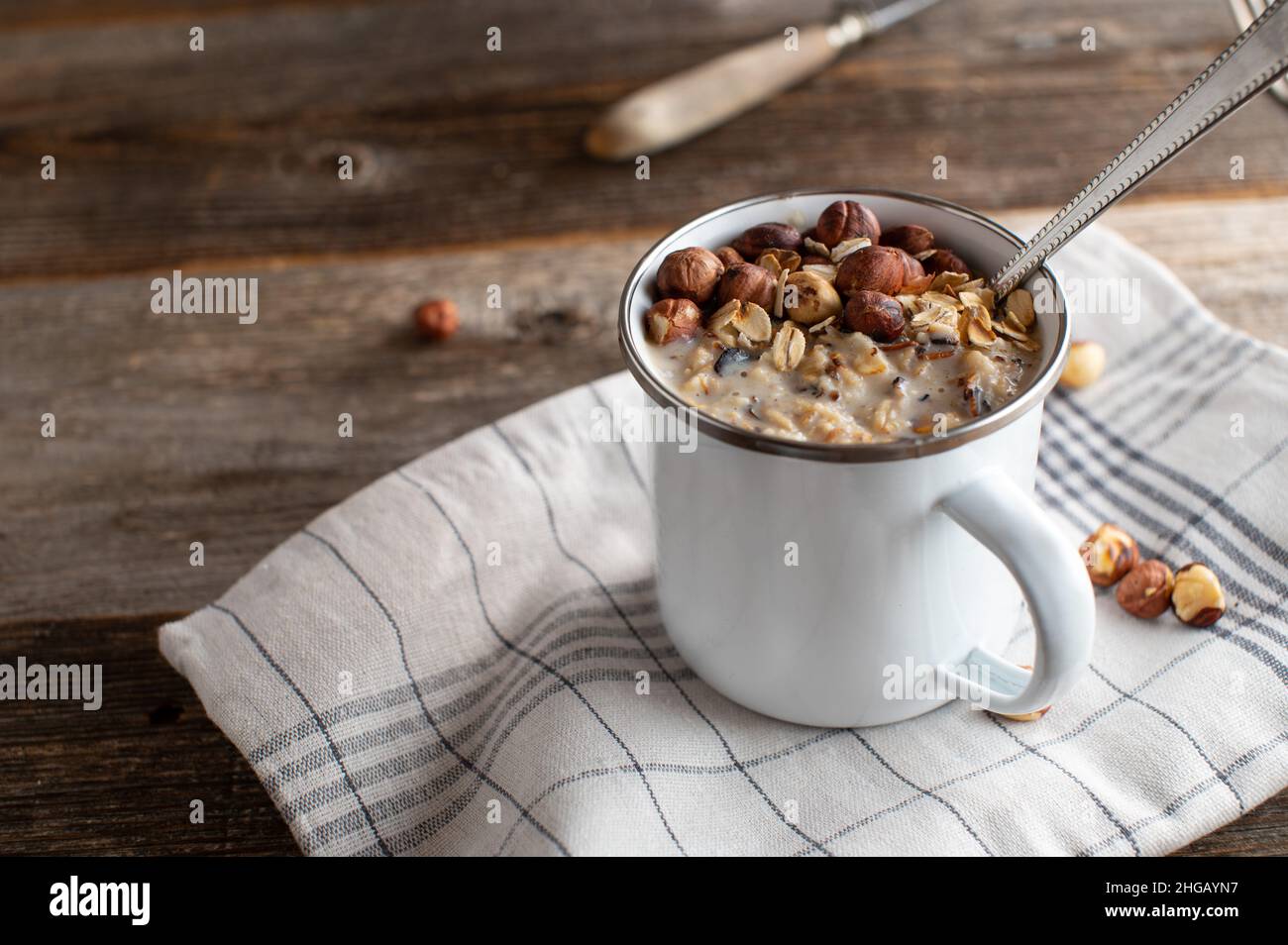 Porridge con nocciole tostate in una tazza di smalto bianco con cucchiaio Foto Stock