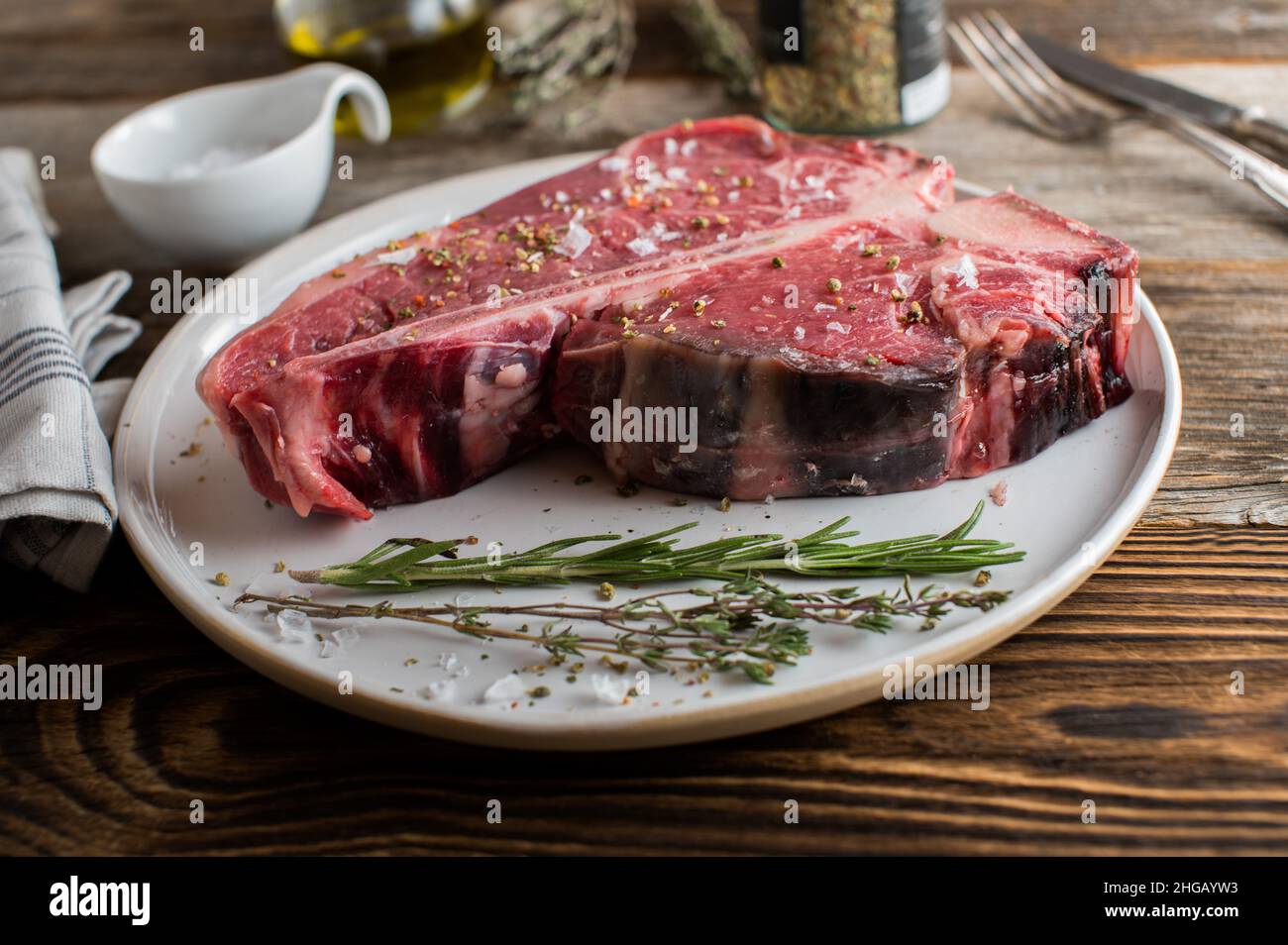 Bistecca di Porterhouse secca invecchiata e cruda con condimento ed erbe aromatiche Foto Stock