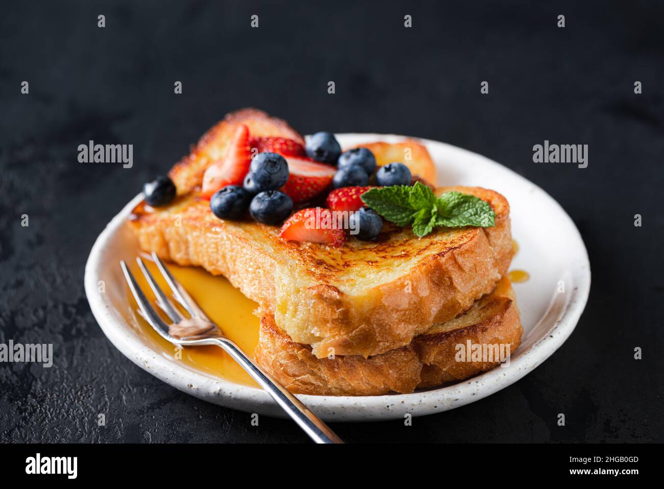 Toast alla francese con frutti di bosco e miele su sfondo nero Foto Stock