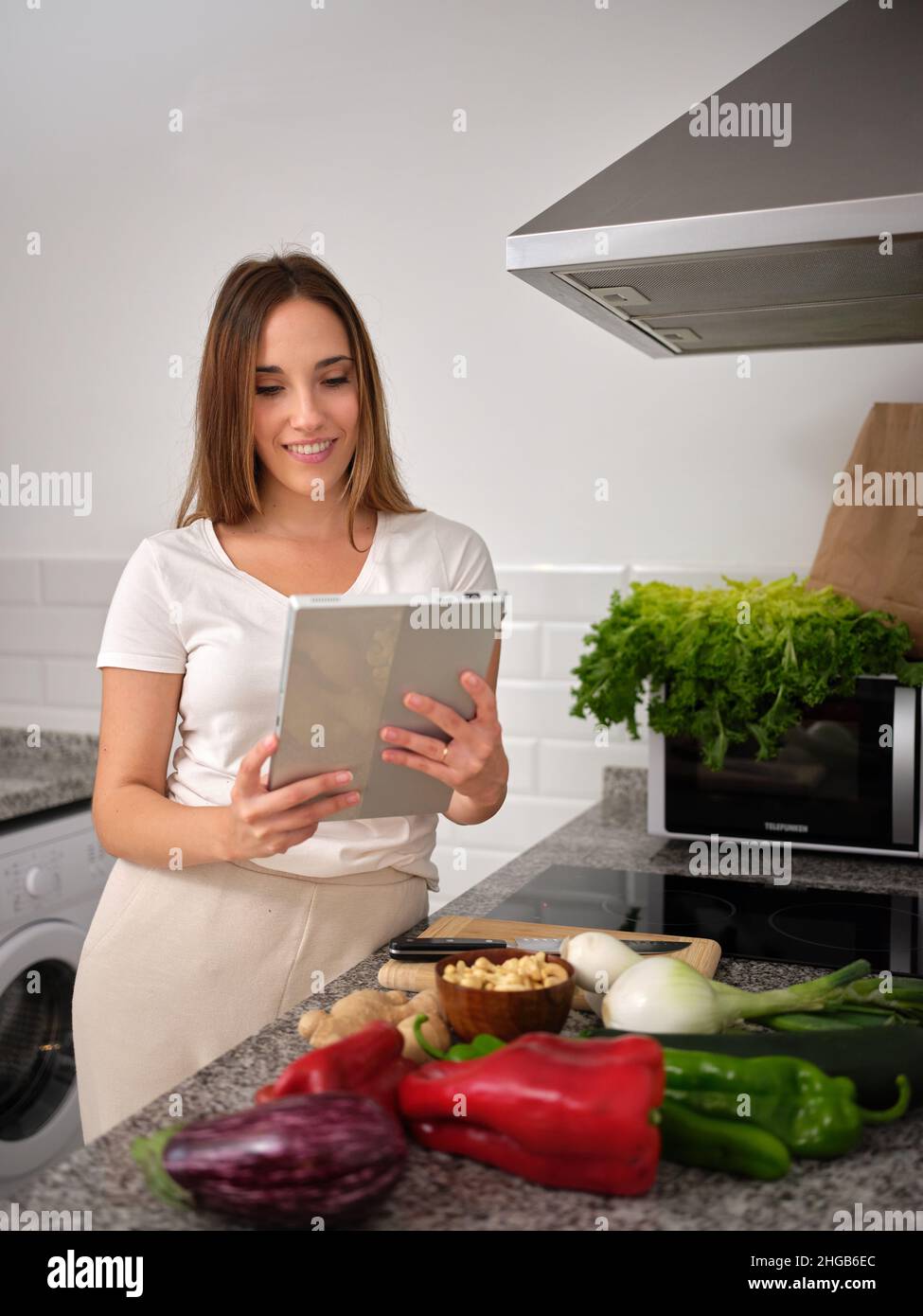 cuoco in cerca di una ricetta vegana sulla sua tavoletta, in piedi davanti al piano di lavoro Foto Stock