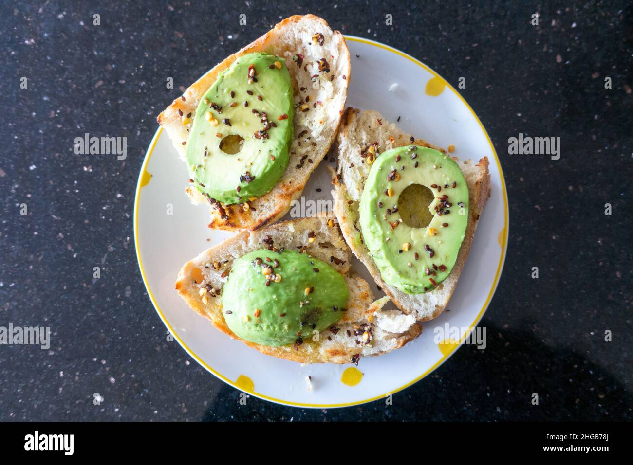 Avocado affettato su fette di pane rustico con semi di sesamo nero e scaglie di peperoncino posto su un piatto vista dall'alto verso il basso Foto Stock