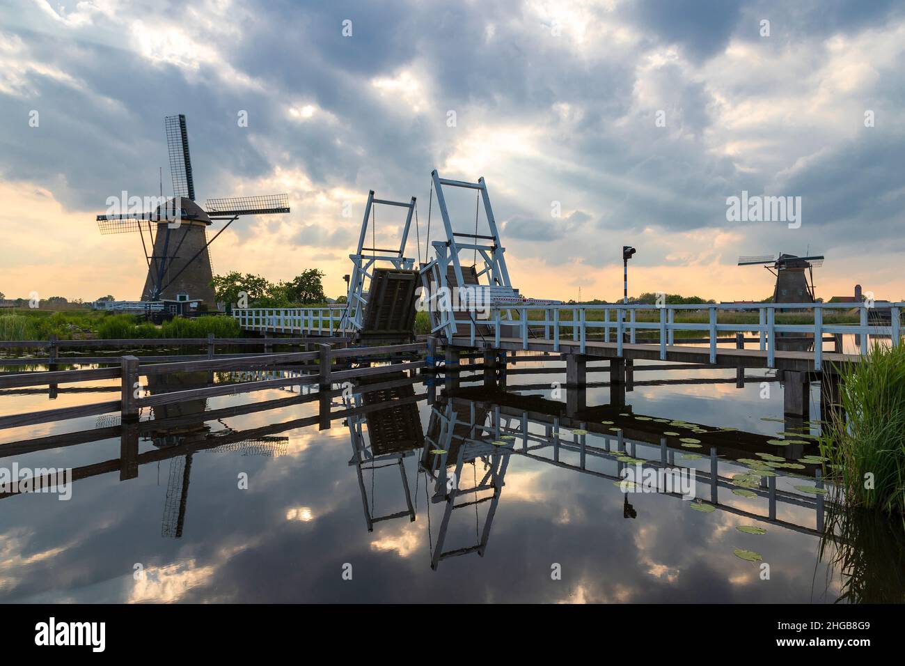 Bellissimo mulino a vento e ponte levatoio su un canale a Kinderdijk in Olanda. Il mulino e le nuvole si riflettono nell'acqua. Ci sono delle nubi drammatiche nel Th Foto Stock