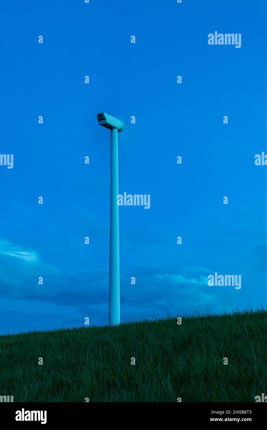Impianto eolico su prato verde. Foto al tramonto a lungo. Ci sono belle nuvole blu nel cielo. Foto Stock