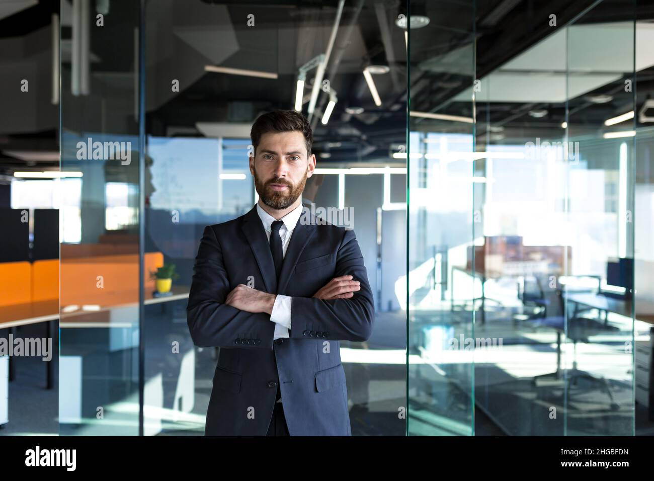 Uomo d'affari di successo maschio che guarda la macchina fotografica con le braccia incrociate, serio imprenditore in ufficio moderno Foto Stock
