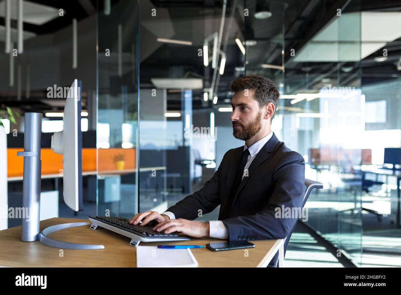 Serio e pensieroso imprenditore maschile che lavora in ufficio al computer in un tuta aziendale Foto Stock