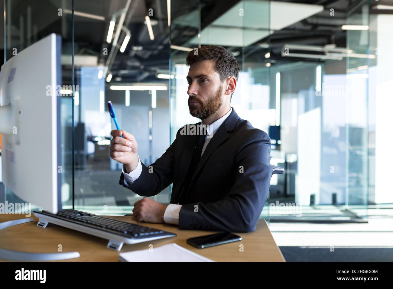 Serio e pensieroso imprenditore maschile che lavora in ufficio al computer in un tuta aziendale Foto Stock