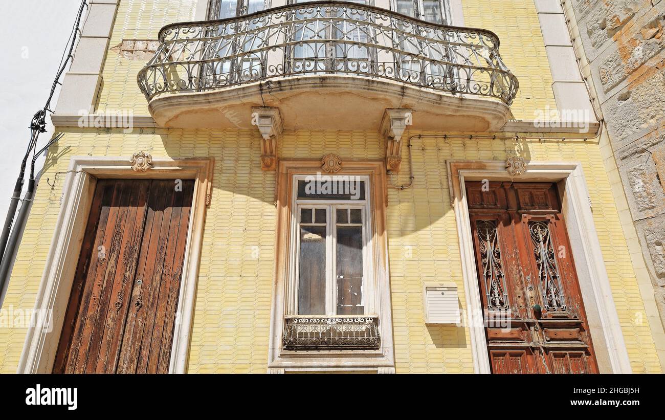 Facciata piastrellata gialla-casa cittadina neoclassica-porte in legno scheggiate-ringhiera in metallo balcone-finestra chiusa. Tavira-Portogallo-067 Foto Stock