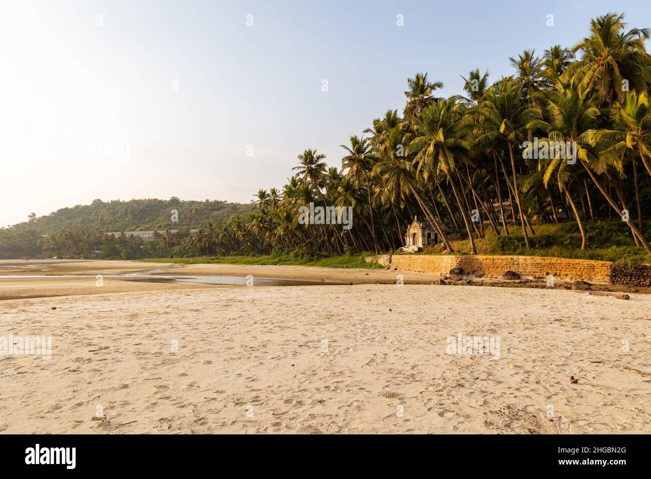 Bella vista di una piccola cappella situata tra alte palme da cocco sulla riva della spiaggia di Velsao vicino a Sankval, Mormugao, Goa, India Foto Stock