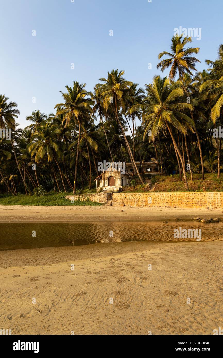 Bella vista di una piccola cappella situata tra alte palme da cocco sulla riva della spiaggia di Velsao vicino a Sankval, Mormugao, Goa, India Foto Stock
