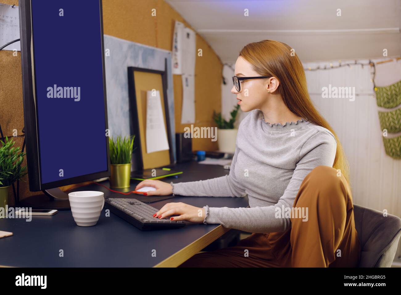 Rimani a casa, una ragazza chic lavora in un'atmosfera familiare. Ragazza freelance che lavora a un computer con occhiali, guardando uno schermo verde su un computer. Il Foto Stock