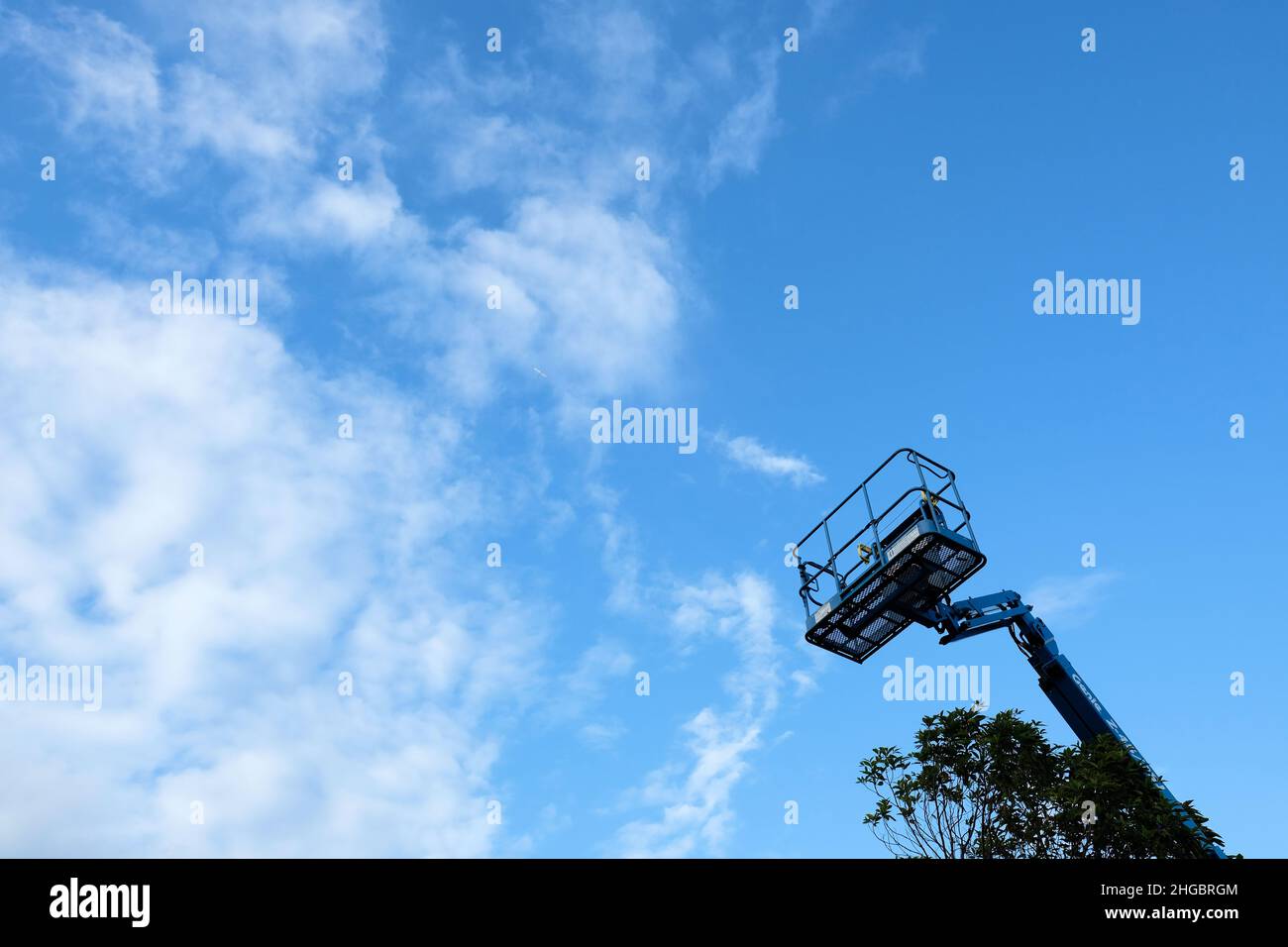 Cestino alla fine di un braccio telescopico Genie con un cielo blu e le nubi di Cirrus wispy sullo sfondo; costruzione industriale, attrezzature di manutenzione. Foto Stock
