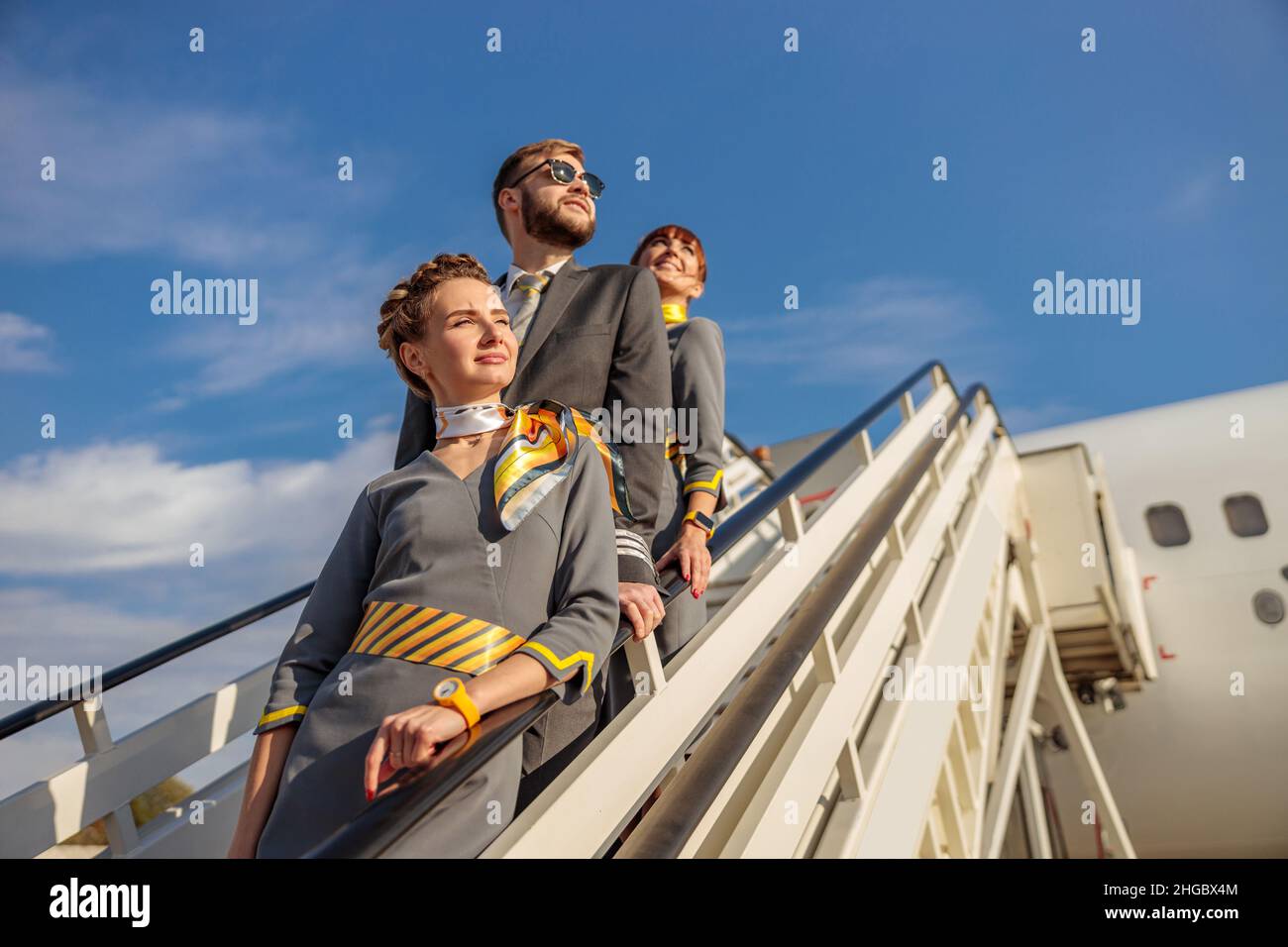 Due donne stewardesses e capitani di aviazione maschile in piedi sulle scale di imbarco aerei sotto il cielo blu Foto Stock