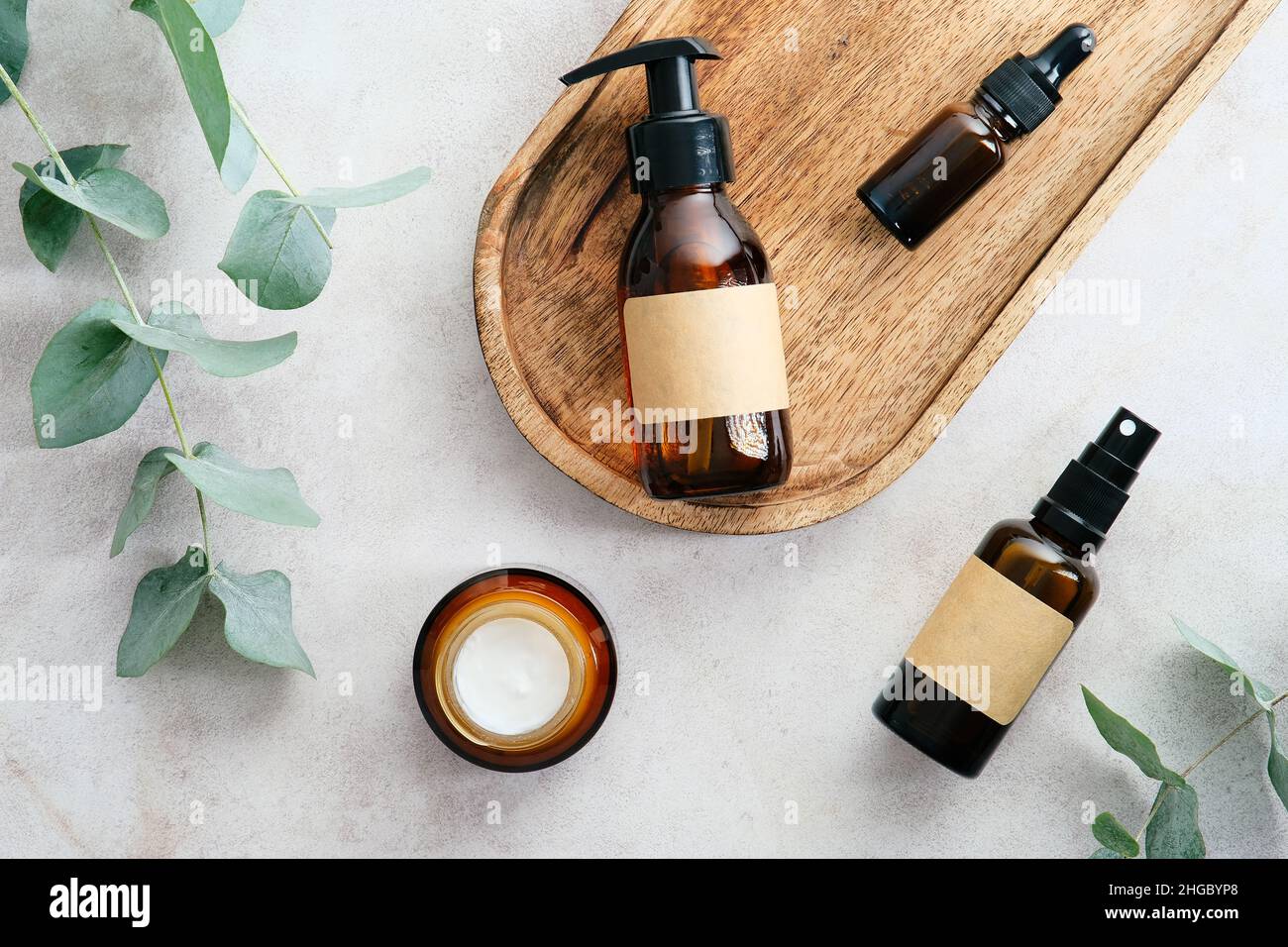 Bottiglie cosmetiche in vetro ambrato scuro con etichette bianche e foglie verde eucalipto su tavola di pietra. Disposizione piatta, vista dall'alto. Foto Stock