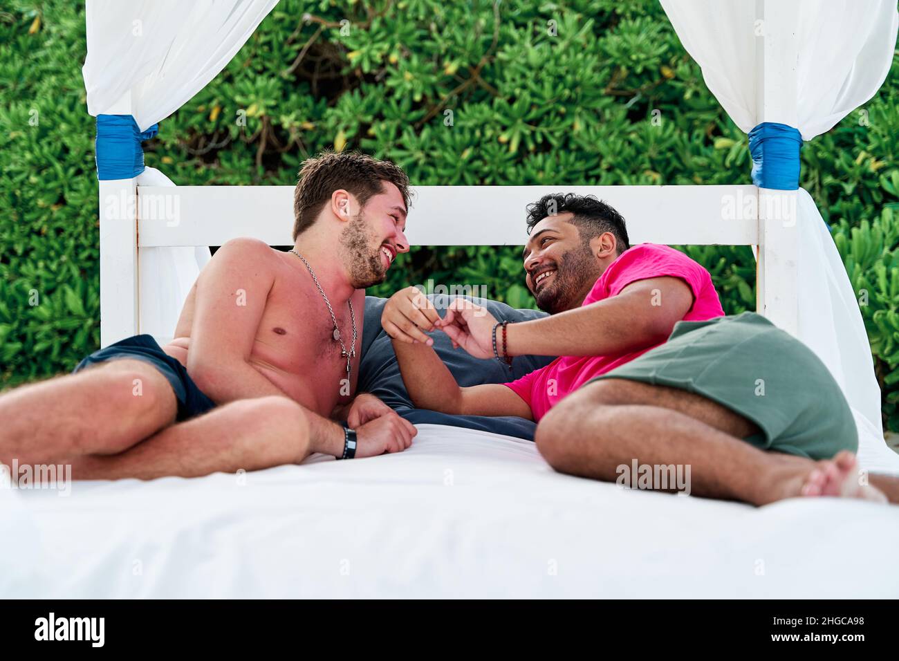 ritratto di una coppia omosessuale di due uomini sdraiati su un lettino da spiaggia in un beach club a cancun mentre si gioca e si ride, concetto lgbti Foto Stock