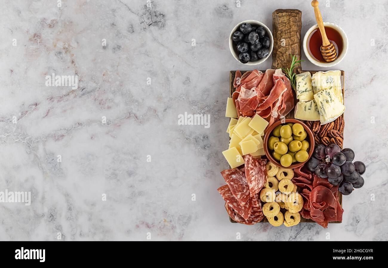 Vista dall'alto di gustosi salumi con formaggio, uva, noci, olive e prosciutto su un piatto da cucina circolare Foto Stock