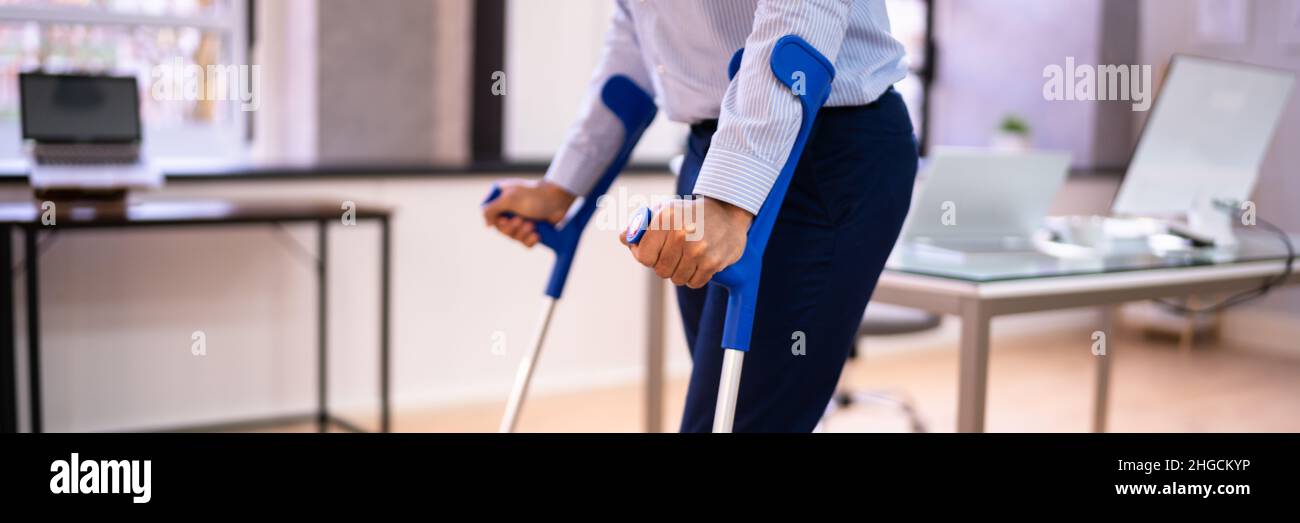 Lavoratore con stampelle sul posto di lavoro o in ufficio. Benefici per la riabilitazione degli handicap Foto Stock