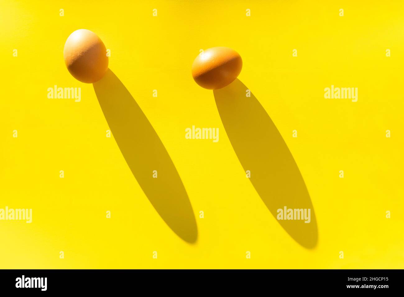 Due uova di fattoria marroni su sfondo giallo in luce brillante, un concetto di minimalismo. Foto Stock