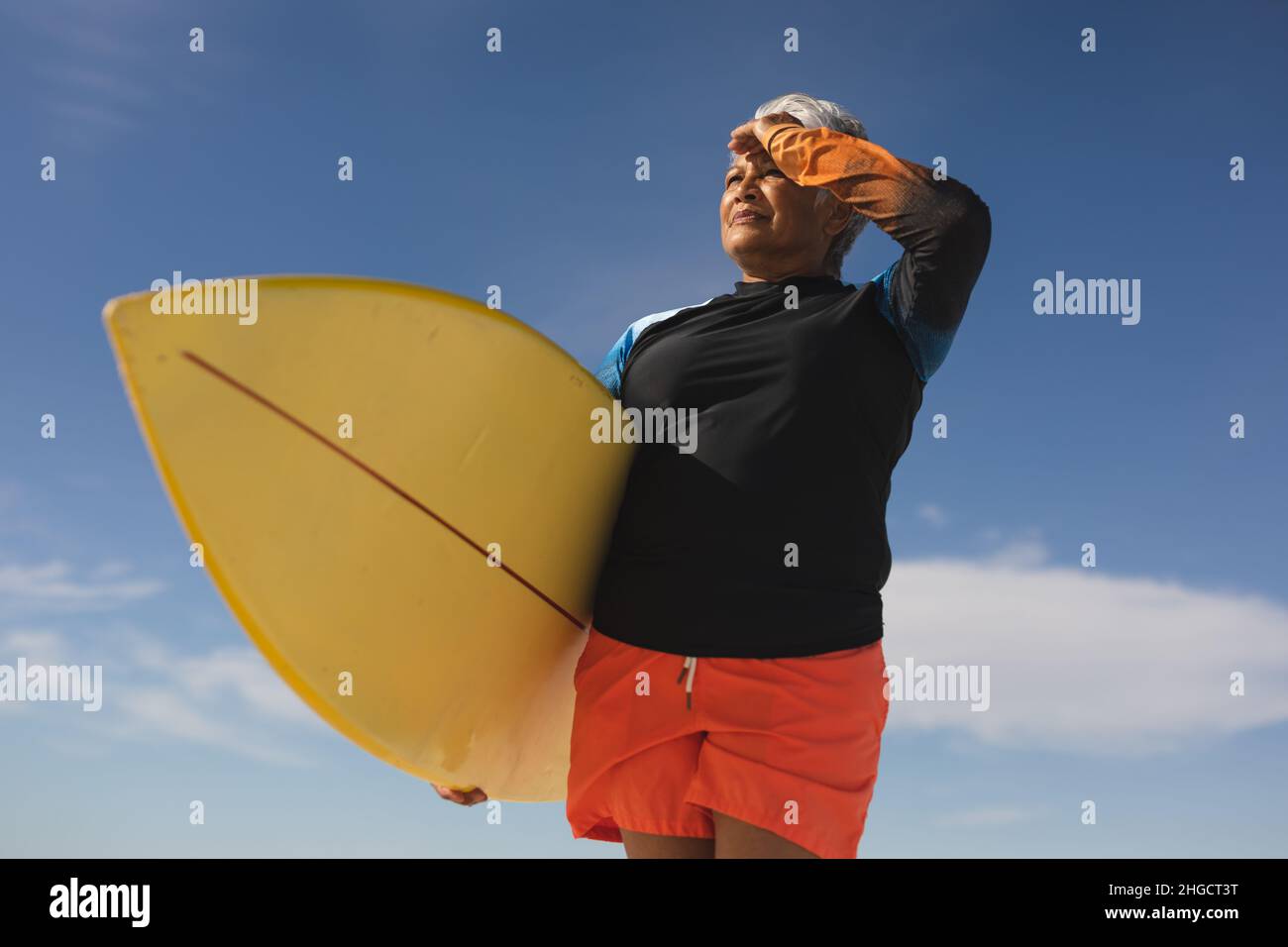 Vista ad angolo basso della donna biraciale con occhi di protezione da surf mentre si guarda lontano dal cielo blu Foto Stock