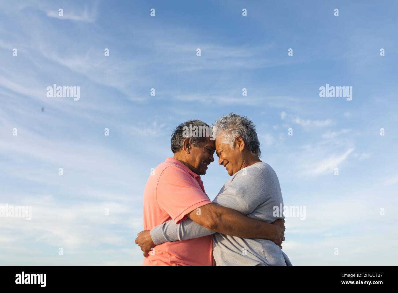 Coppia anziana biraciale amorevole che si abbraccia mentre si toccano le fronte contro il cielo Foto Stock